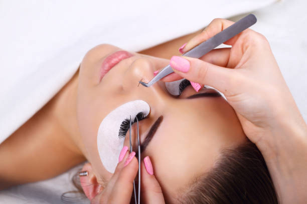 Lash Extension Application Close-Up: A woman receiving professional eyelash extensions, focused on meticulous application using tweezers.